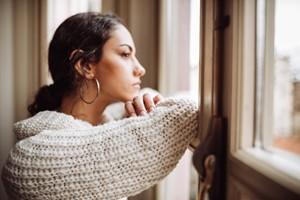 young pensive woman leaning on window and gazing out
